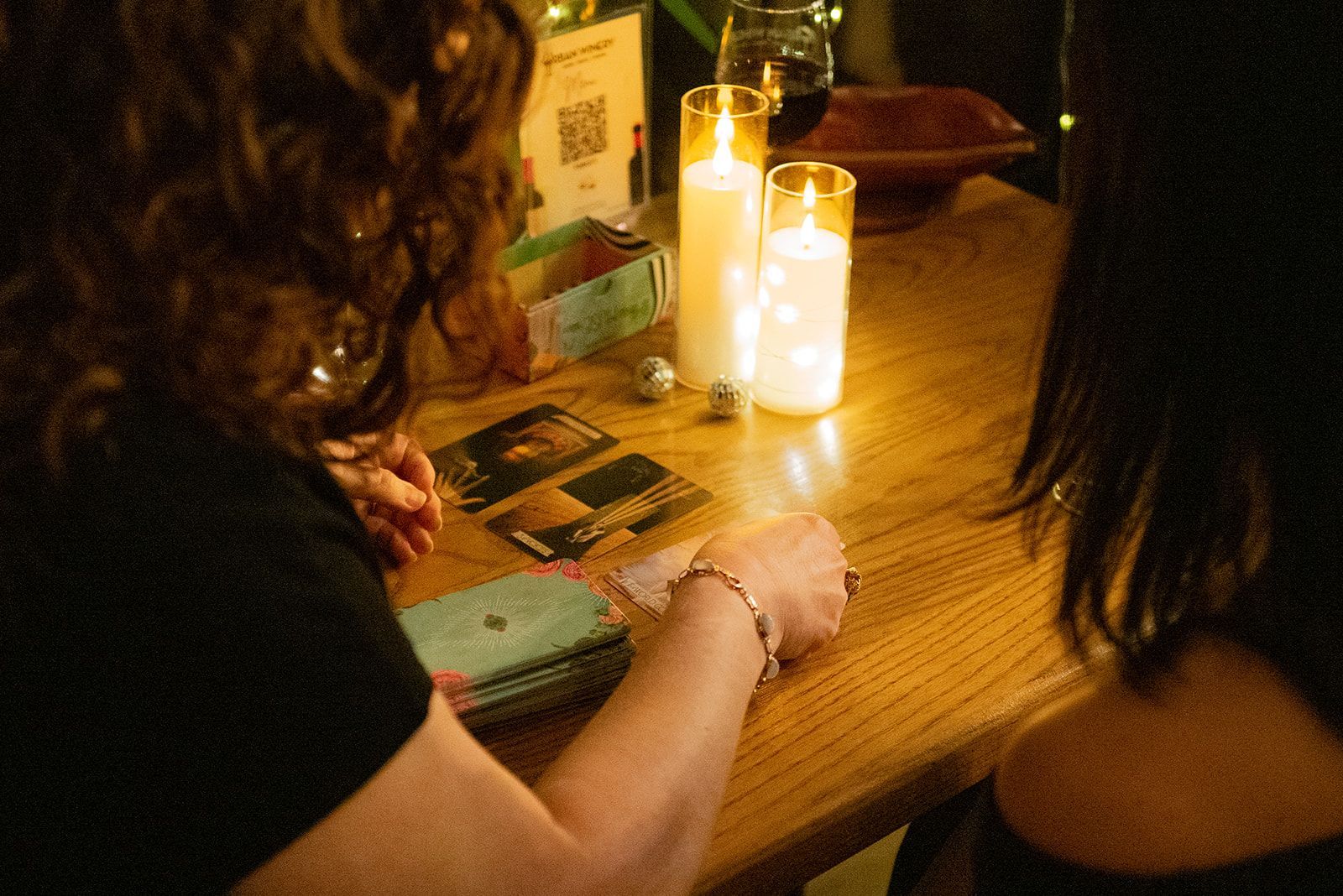 Two people sit at a candlelit wooden table with cards and a phone, creating a cozy, dim atmosphere.