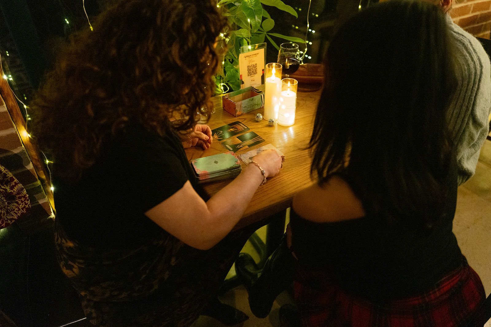 Two people sit at a candlelit table, writing or drawing on papers with drinks and plants nearby.