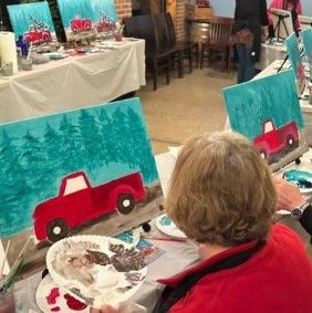 Person painting a red truck on canvas at a craft workshop