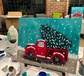 Red pickup truck painting with a snowy pine tree, set on an easel with art supplies nearby