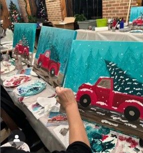 People painting red truck winter scenes on turquoise canvases at a craft table