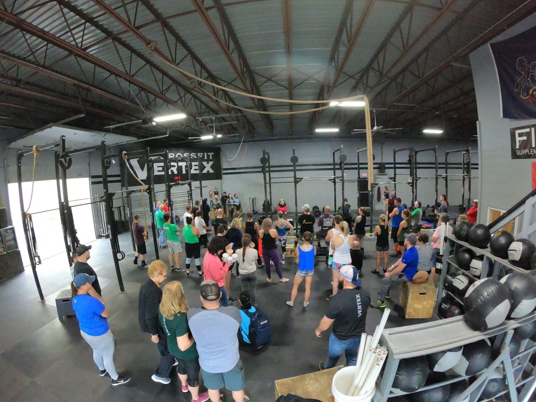A group of people are standing in the gym at CrossFit Vertex during a CrossFit competition