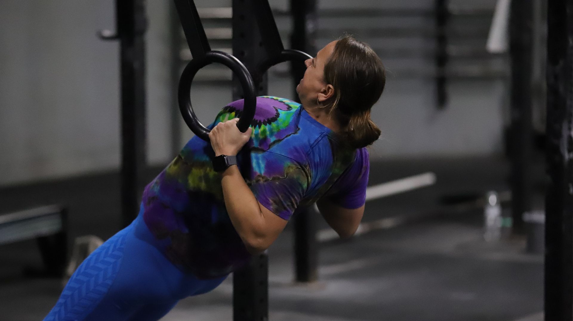 A woman is doing pull ups on gymnastic rings in a gym.