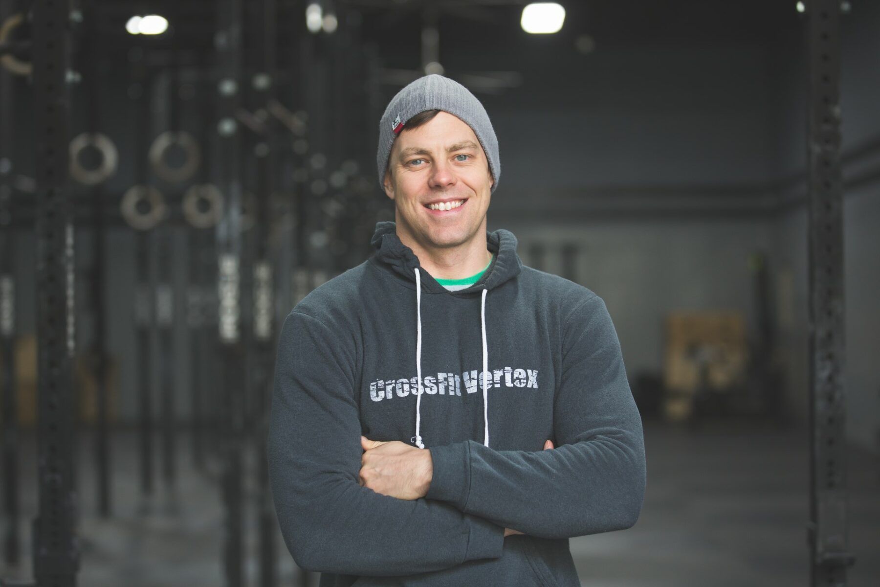 A man wearing a CrossFit Vertex hoodie and a beanie is standing in a gym 