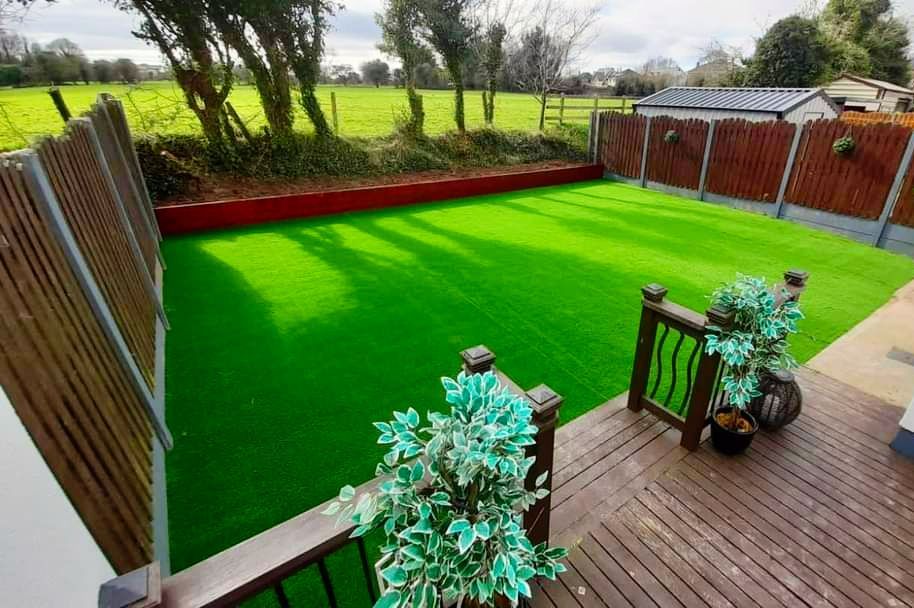 A backyard with bright green artificial turf, surrounded by wooden fences and a deck with potted plants.