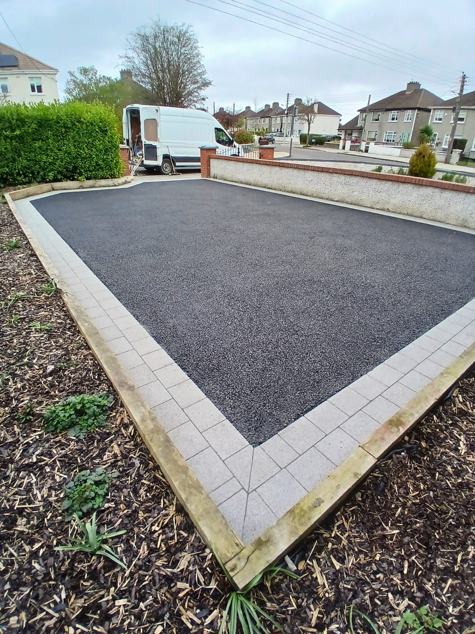 Black gravel bocce ball court with brick border and wooden edging. A van is parked nearby.