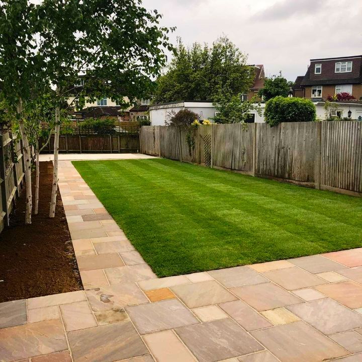 A well-manicured backyard with a stone patio, lush green lawn, and wooden fence.