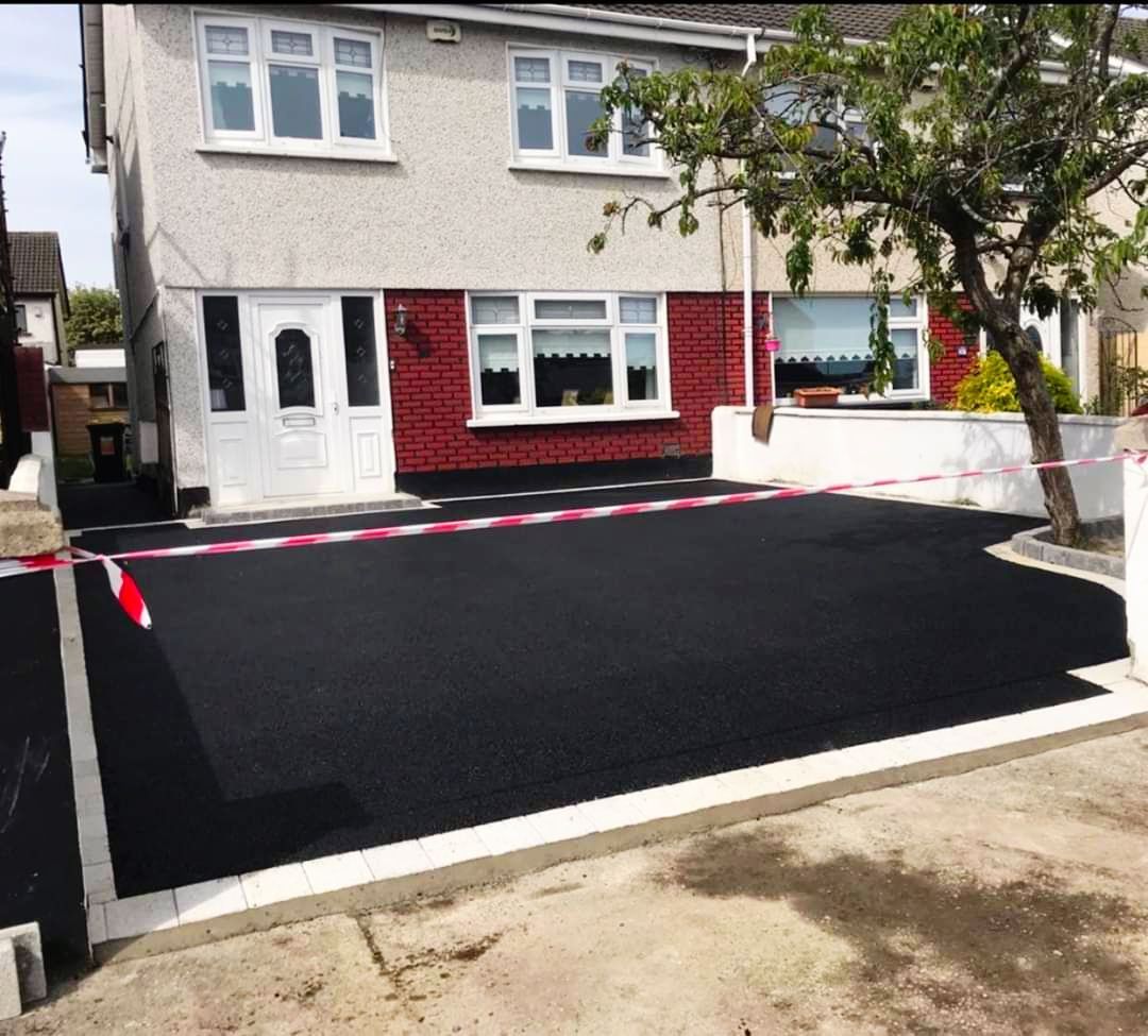 A two-story house with a newly paved black driveway bordered by white pavers.