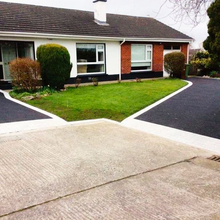 Exterior view of a house with a small lawn, black paved driveways, and concrete apron.
