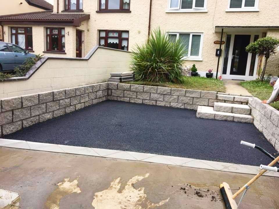 Asphalt driveway enclosed by stone walls, with a house in the background.