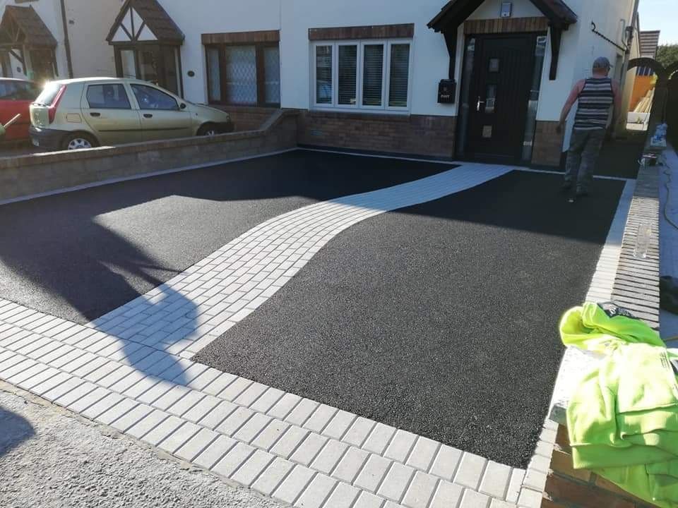 Black asphalt driveway with light brick border and a white-brick stripe, front of a house.