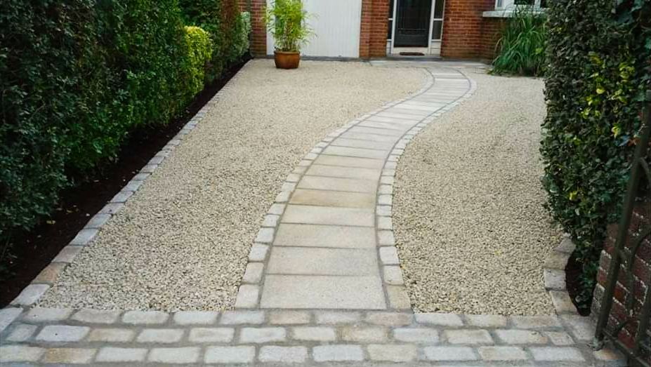 Stone pathway curves through a gravel driveway, flanked by green hedges.