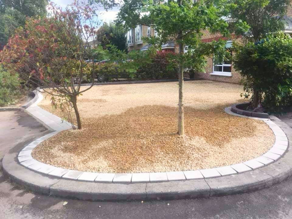 Gravel bed with trees and a concrete border in a circular shape. Houses are in the background.