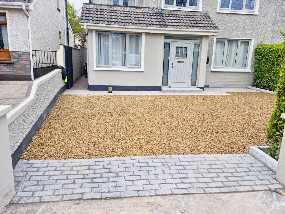 Gravel driveway in front of a light-colored house with a brick-paved walkway.