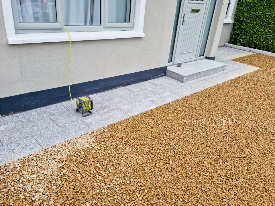 Exterior view of a house entrance with a grey stone pathway and a gravel driveway.