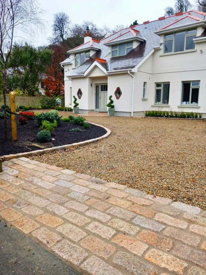 White house with gravel driveway and brick walkway. Landscaping with dark mulch and green plants.