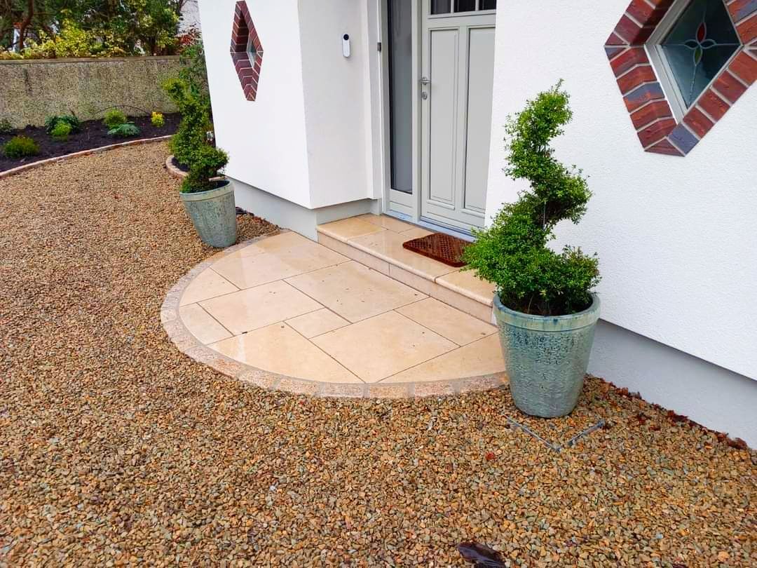 Entrance with curved stone patio, gravel, and potted topiary.