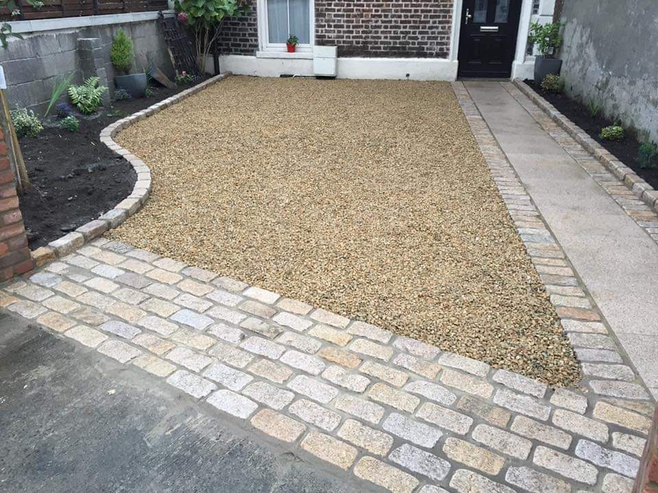 Gravel driveway framed by brick edging, walkway, and small flowerbeds in front of a brick house.