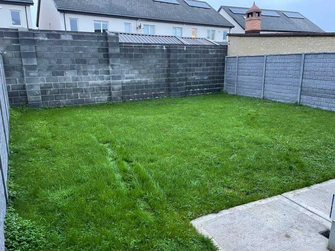 Green grassy backyard bordered by concrete block walls, adjacent to a house.