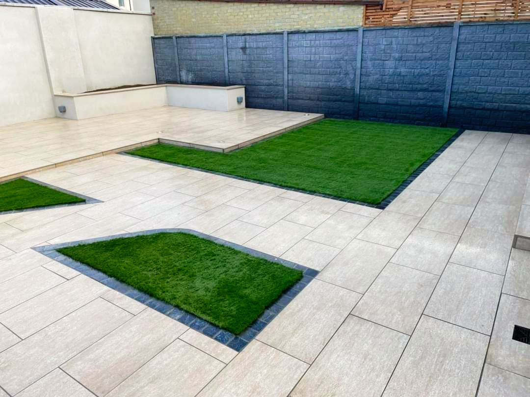 Modern patio with light stone pavers, artificial turf patches, and gray concrete walls.