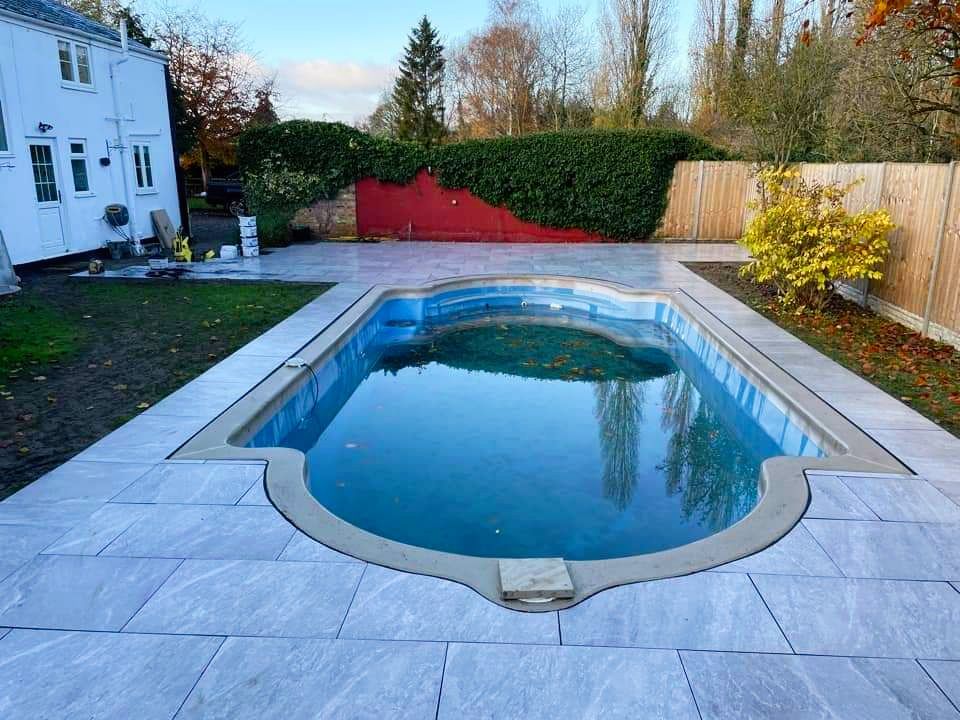 Swimming pool with blue water surrounded by stone patio.