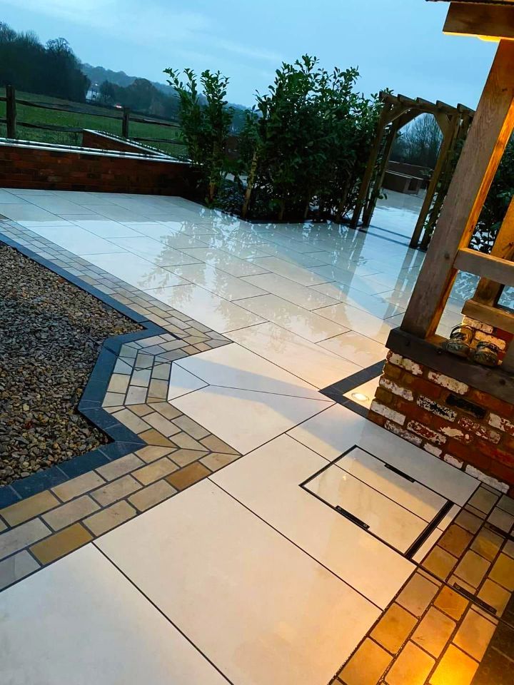 Outdoor patio with light-colored tiles, brick accents, and a wooden archway. Wet surface, overcast sky.