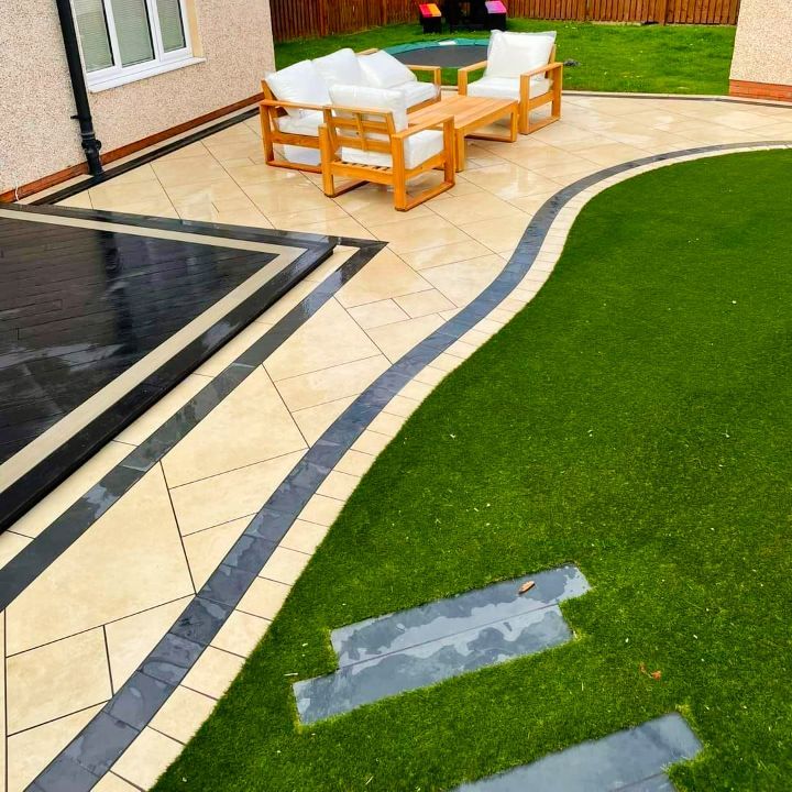 Patio with beige and black pavers, wood furniture, and green lawn.
