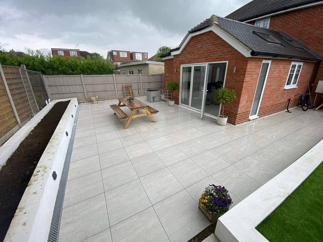 A paved patio with a brick house, table, and planter box. Overcast day.