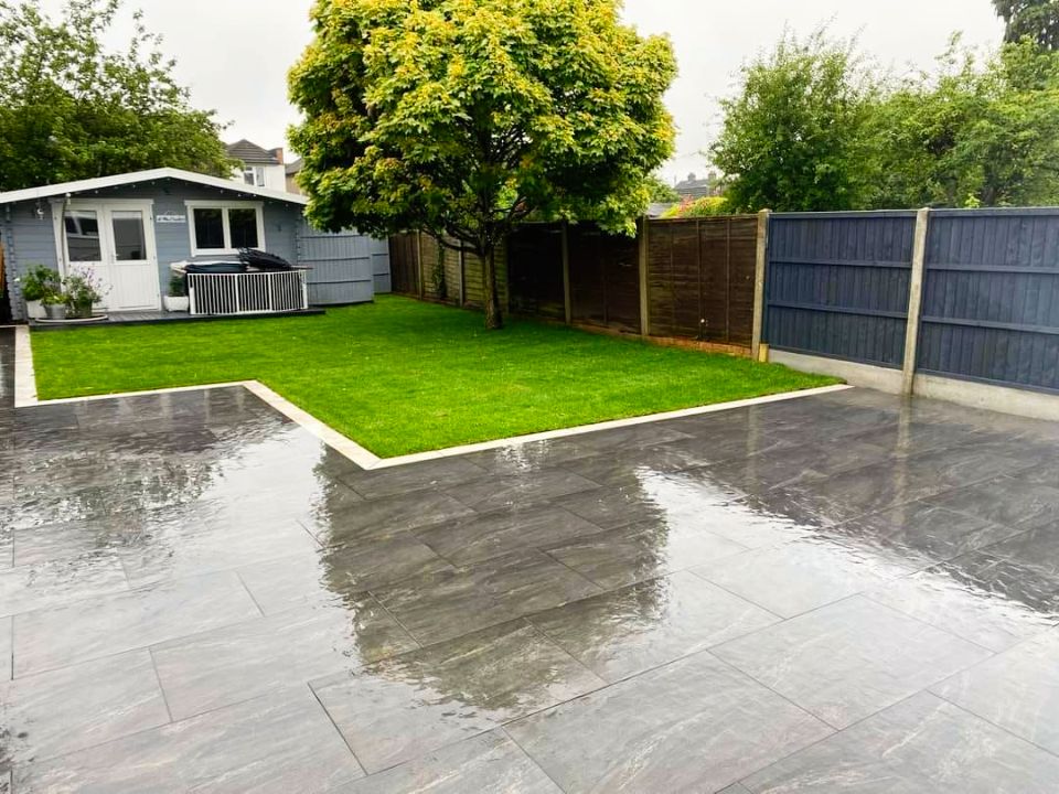 Patio and lawn with wet, gray stone tiles, green grass, and a blue shed in the background.