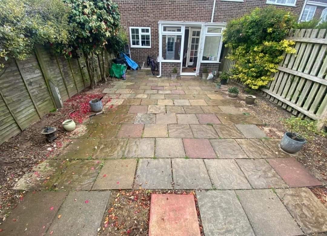 A small backyard with stone patio, surrounded by fences and greenery, leading to a house entrance.
