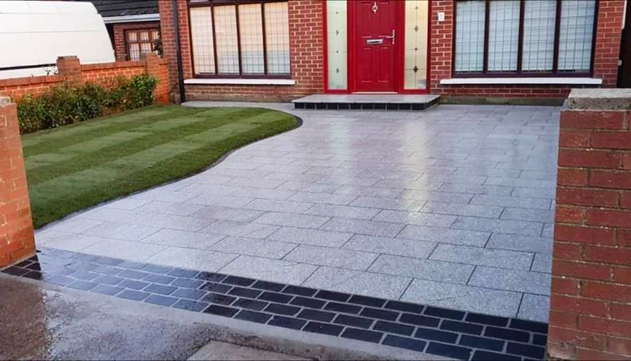 Driveway paved with gray blocks, edged in dark brick. Green lawn to the left, red door in the background.
