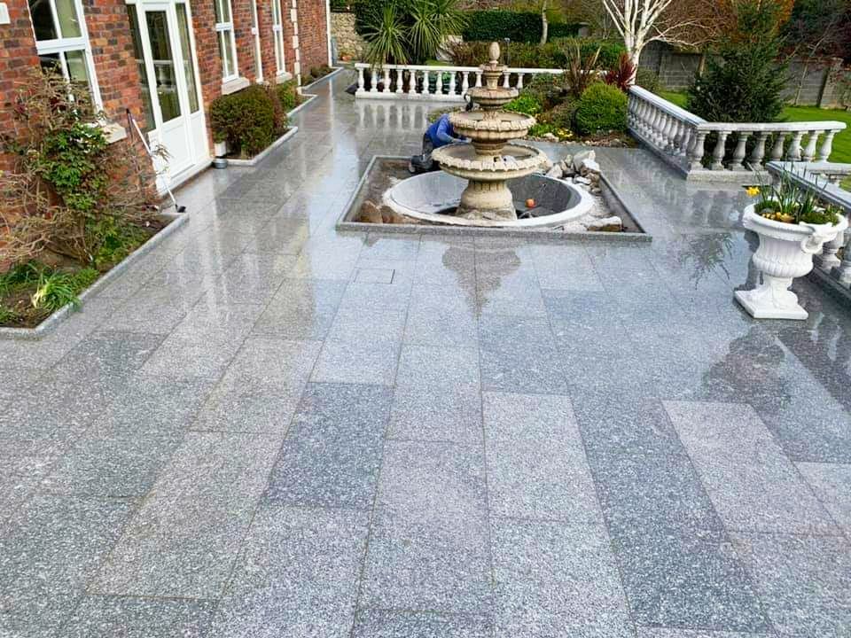 Gray granite patio with a fountain and a person working on it.