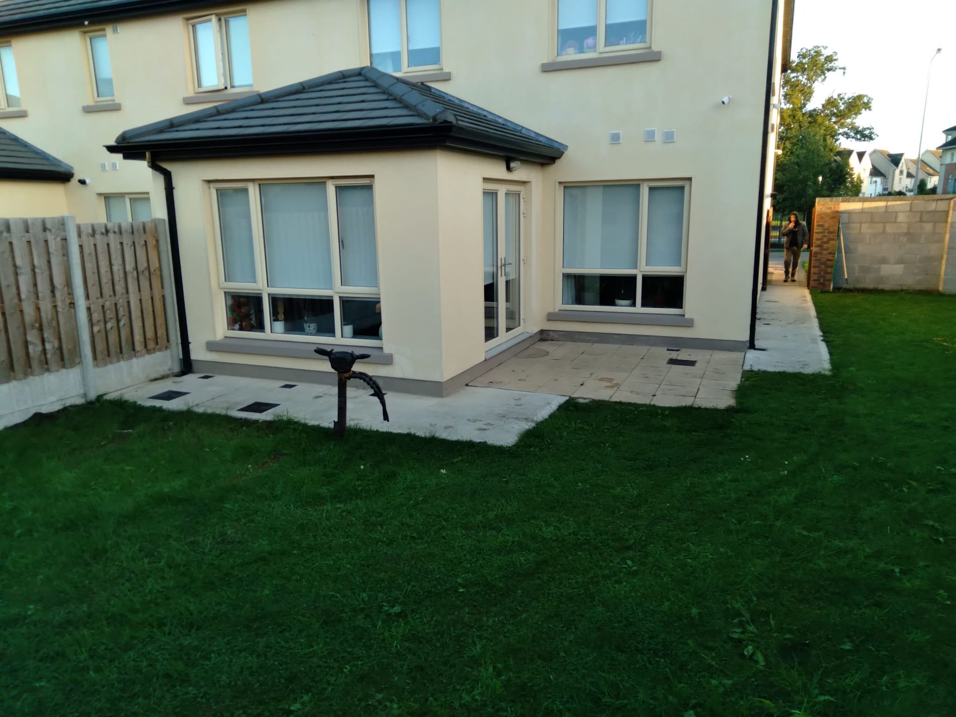 Beige house with glass windows and a small patio area. Green lawn in the foreground.