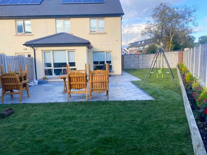Backyard with patio, lawn, wooden furniture, and a swing set; house in the background.