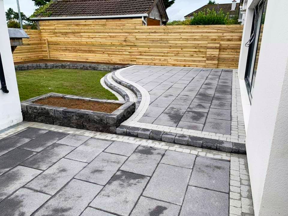 Patio with gray pavers, small lawn, stone retaining walls, and wooden fence.
