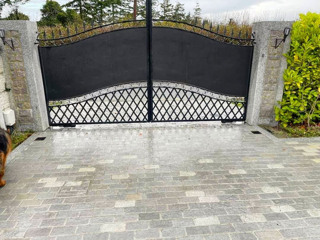 Black metal gate on a gray stone driveway with decorative top and lattice detail.