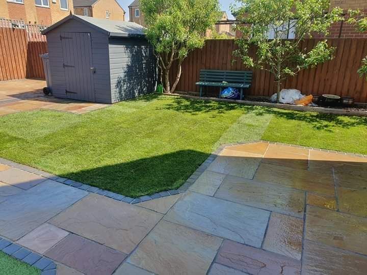 A backyard with a patio, lawn, shed, bench, and trees. Sunny day.
