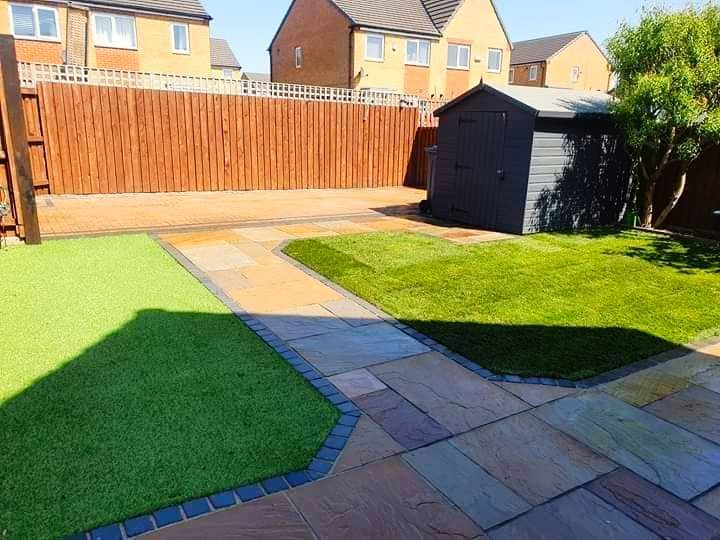 Backyard with green lawn, paved pathways, and wooden fence. A shed sits near the fence.