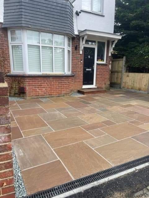 A brick house with a paved driveway in brown flagstones, a black door, and a drainage channel.