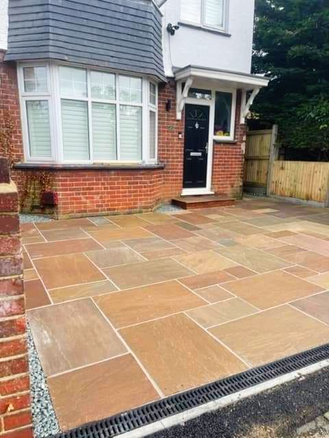 Driveway paved with reddish-brown rectangular stones in front of a brick house with a bay window and black door.