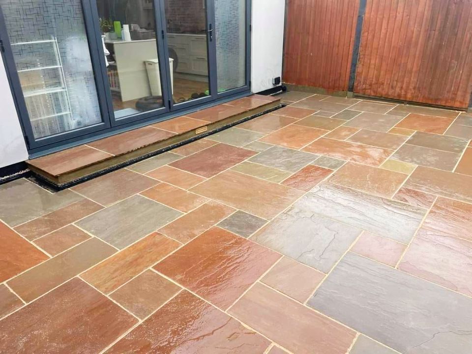 Multi-colored sandstone patio outside a building with glass doors and wooden fencing.