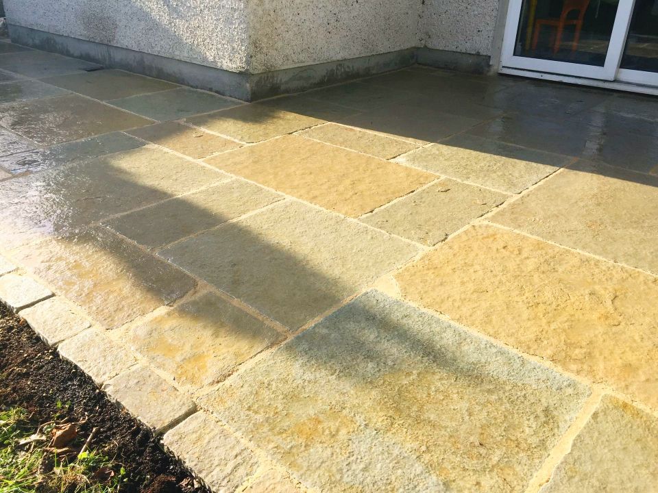 Yellow sandstone patio with wet surface, next to a building and lawn.