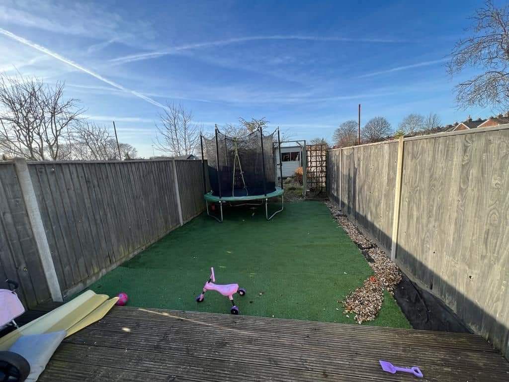 Backyard with a trampoline, artificial turf, wooden fence, and blue sky.