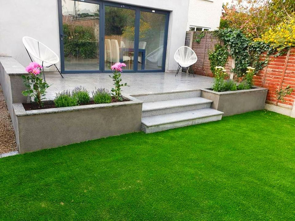 Backyard with green artificial turf, concrete steps and planters, and a glass door.