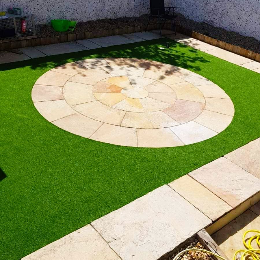 Backyard with circular stone patio surrounded by green artificial turf.