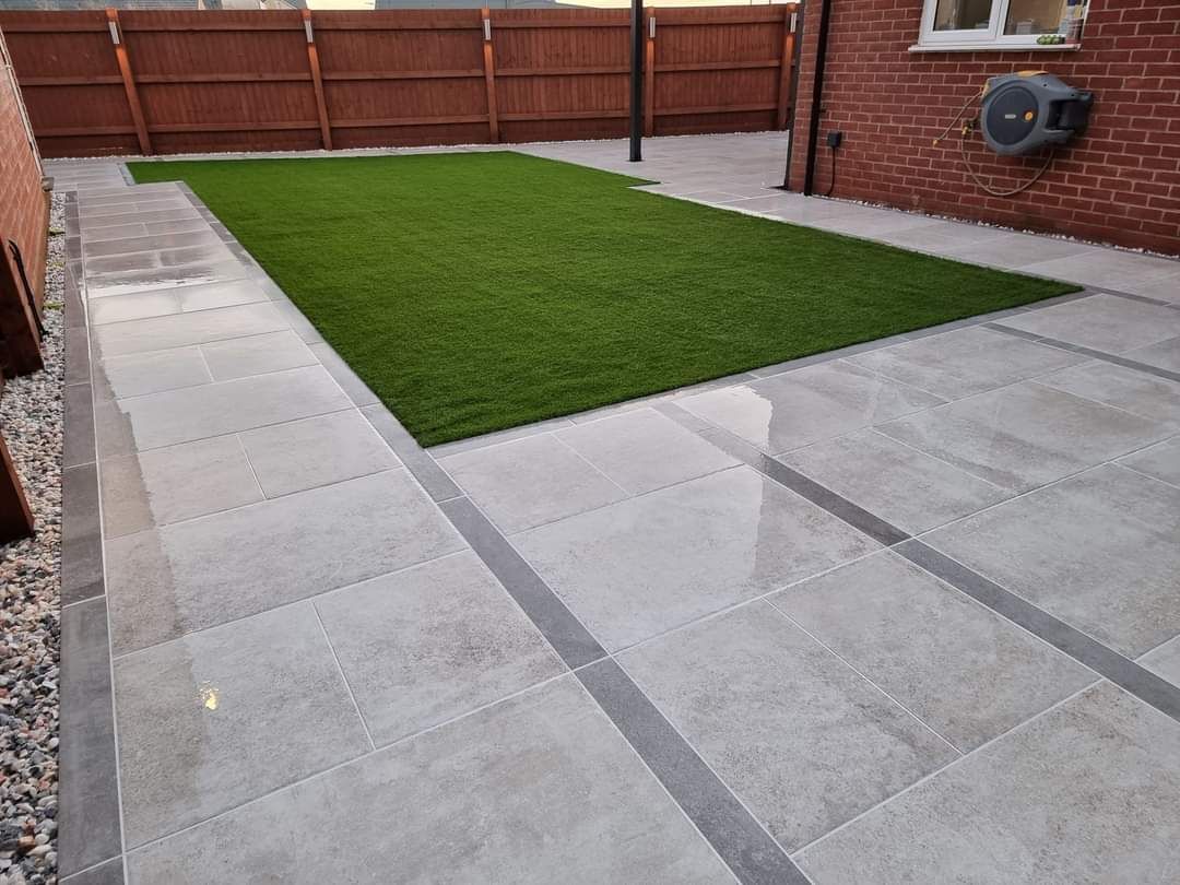 Patio with light gray paving stones, a strip of dark gray, and a patch of green artificial turf.