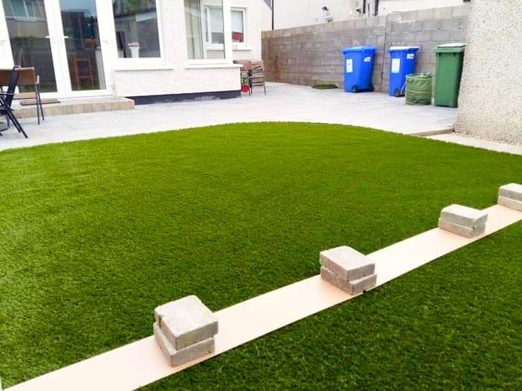 Backyard with artificial green grass, concrete path, and house in background.
