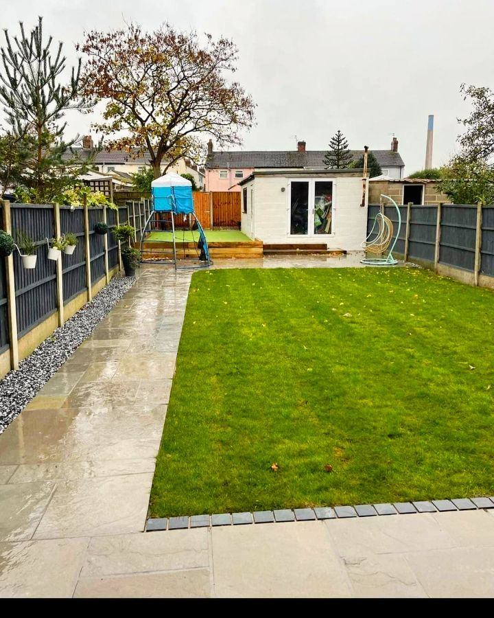 A green lawn with gray stone pathway and a white shed in a backyard with a dark gray fence.