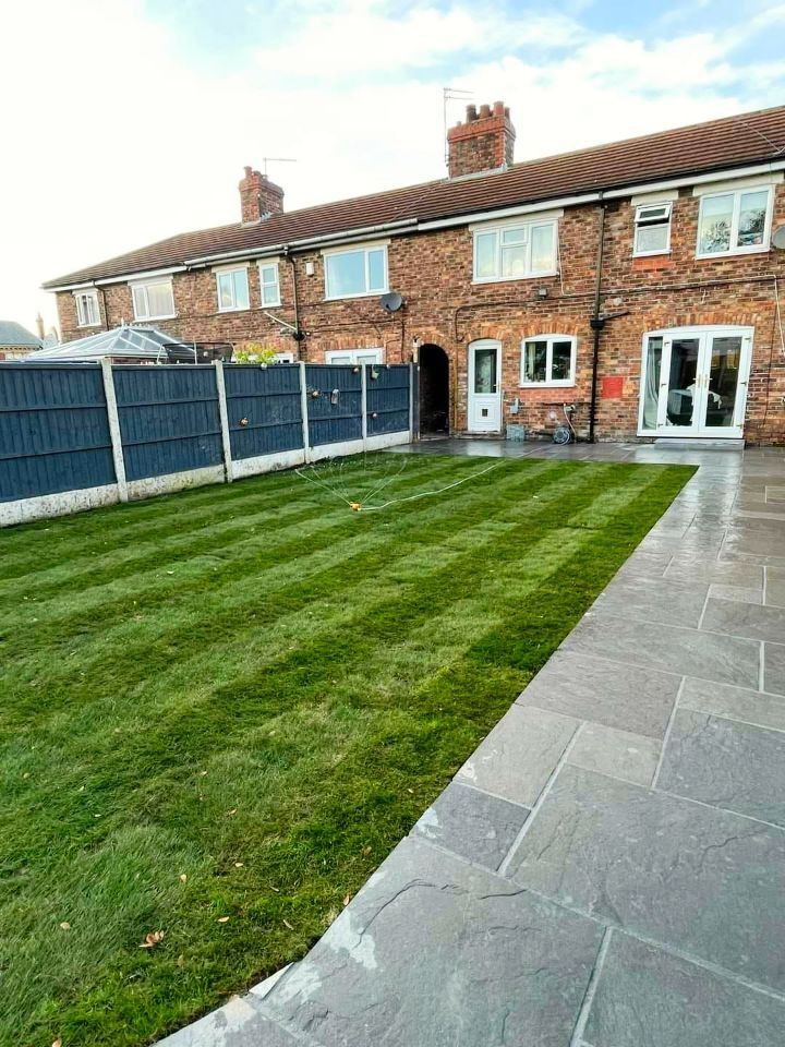 Well-manicured backyard with a striped lawn, dark fence, and brick row houses.