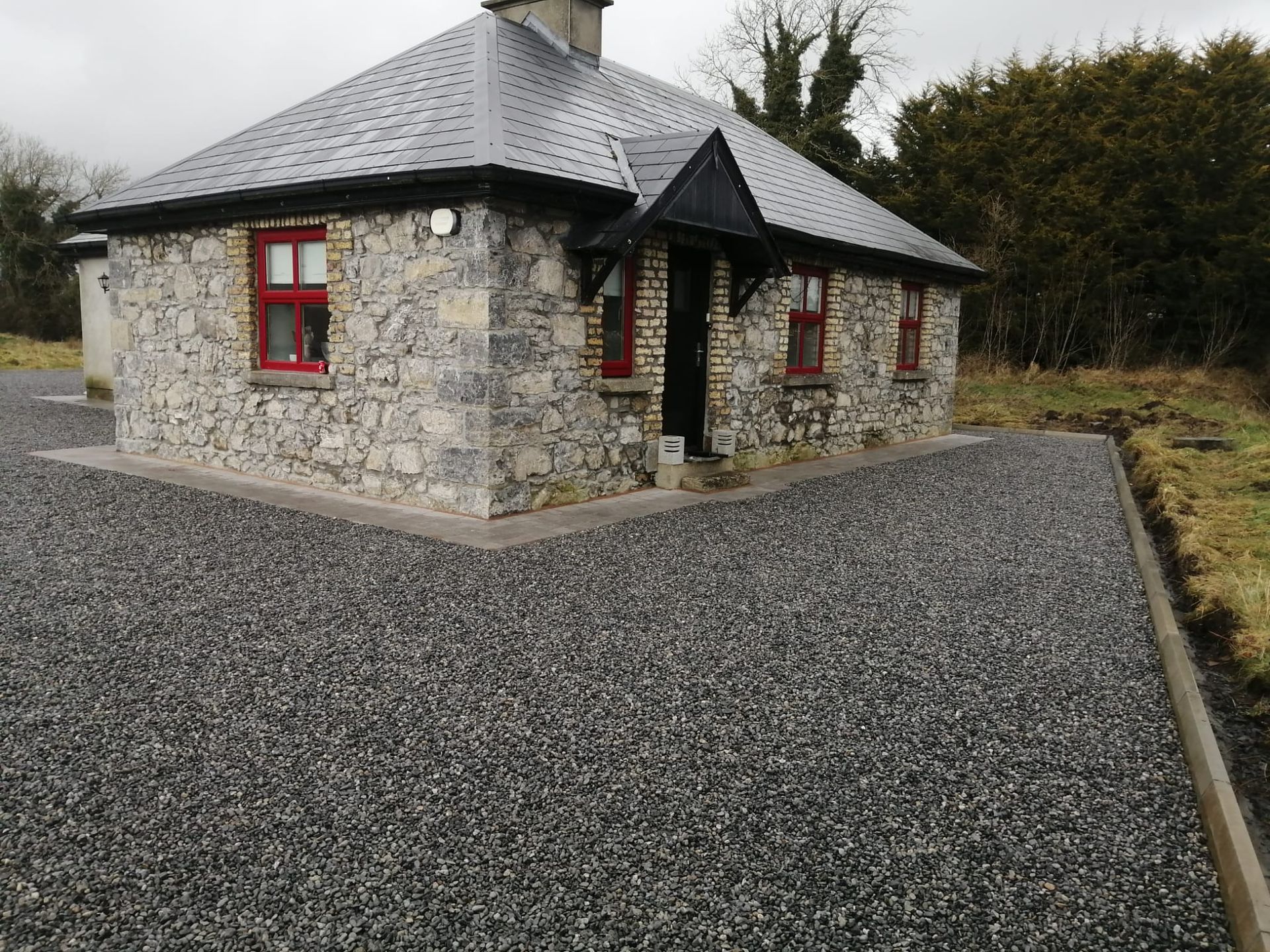 Stone cottage with red window frames and dark gray gravel driveway.